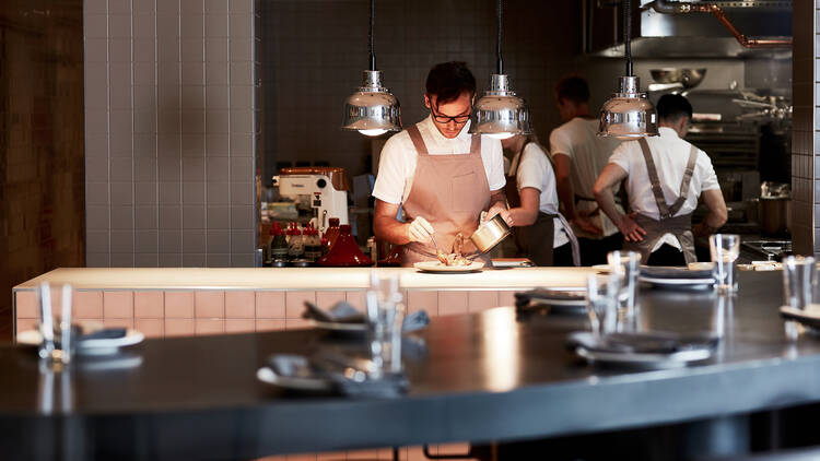 You can see into the open kitchen where a chef spoons sauce onto a plate