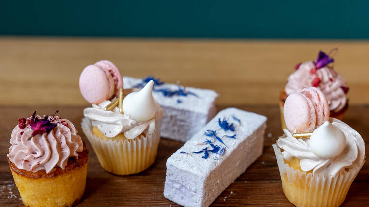 A wooden platter with a selection of tiny cupcakes and marshmallows.