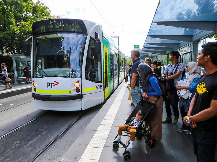 A group of people waiting at a tram stop as a tram pulls up.