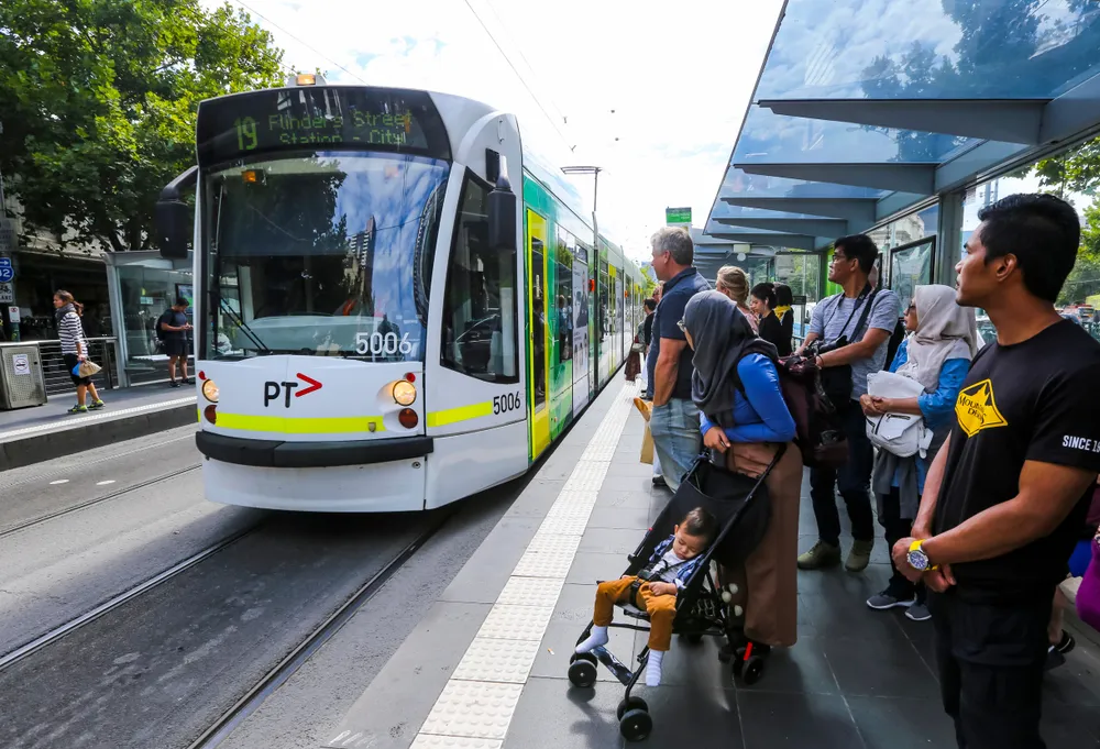 A group of people waiting at a tram stop as a tram pulls up.