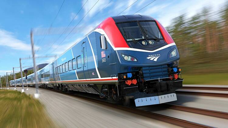 A red and blue train speeds along under a cloudy sky, the trees beside it a blur.