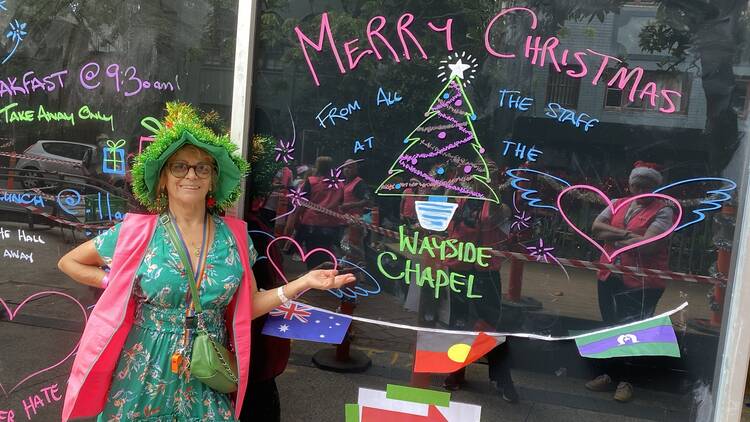 Woman in festive hat standing in front of Christmas messages at Wayside Chapel Kings Cross