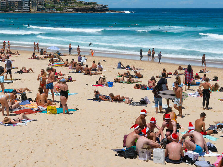 People sitting on Bondi Beach wearing Santa hats.