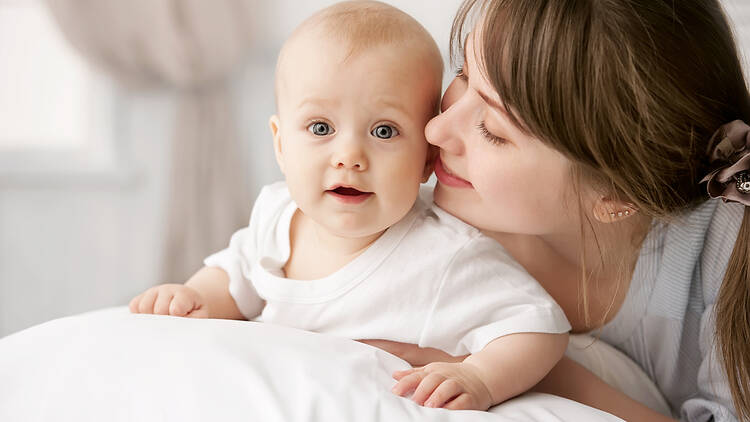 A mother whispers sweet nothings into her baby's ear as it lies on a pillow.