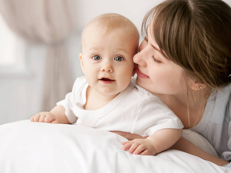 A mother whispers sweet nothings into her baby's ear as it lies on a pillow.