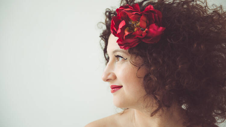 The singer Svetlana in a portrait with a red flower in her brown curly hair.