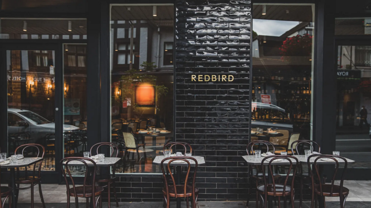 The outside of Redbird Chinese with black tiles and wooden tables and chairs