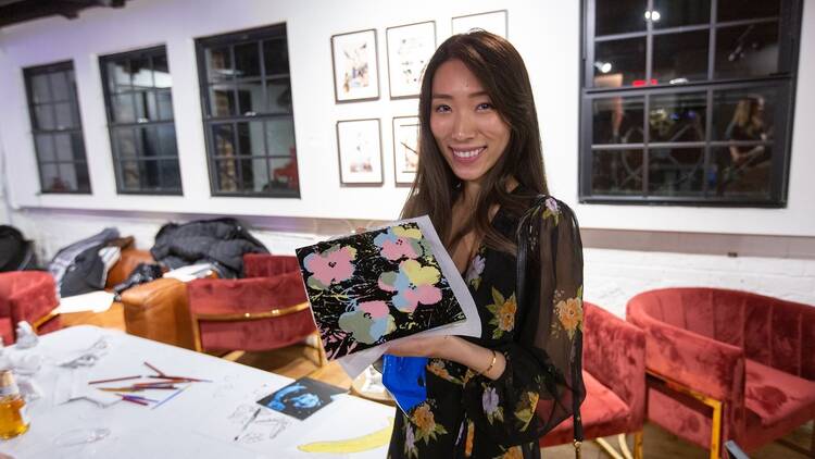 A woman holds up a screenprint version of Warhol's Flowers.