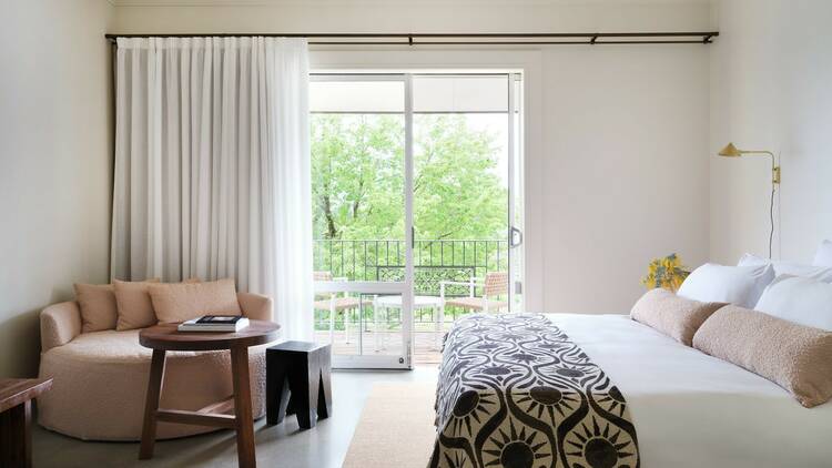 A light, bright hotel room with a bed, side table, daybed and balcony.