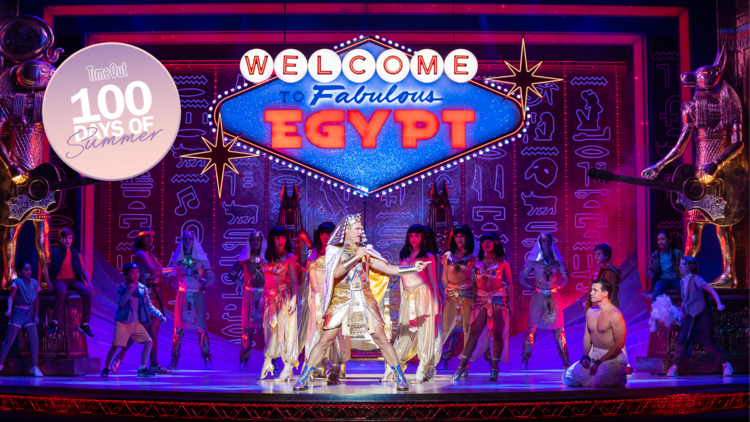 A person dressed as a Pharaoh singing on stage in front of a neon sign that says 'Welcome to Fabulous Egypt'.