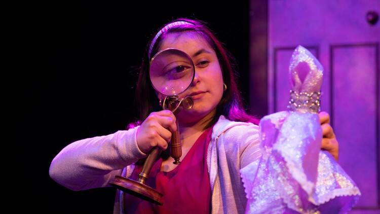 A performer holds up a magnifying glass to her eye.