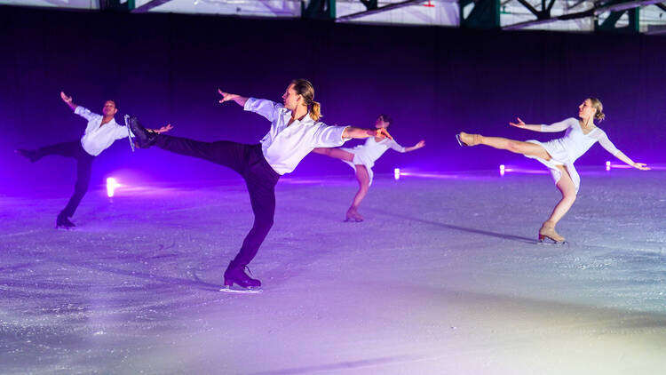 Four ice skaters spin, each with one leg in the air. 