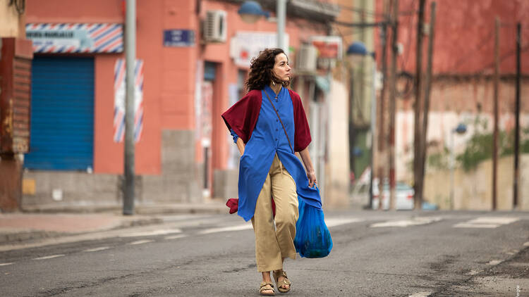 A still from a movie, showing a woman walking along a street. 