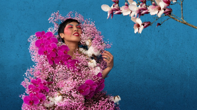 A woman covered in flowers poses against a blue background