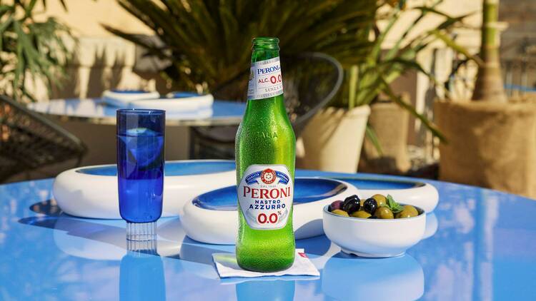 A bottle of Peroni beer on a blue table next to a bowl of olives.