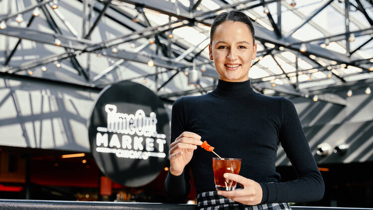 A person standing with a cocktail in front of Time Out Market Chicago sign.