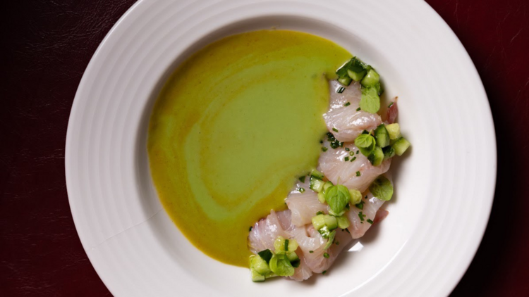 A plate of sliced raw fish with green sauce in a white bowl.