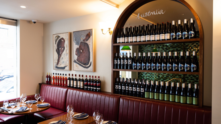 Deep red booth seating below a wall filled with wine bottles.