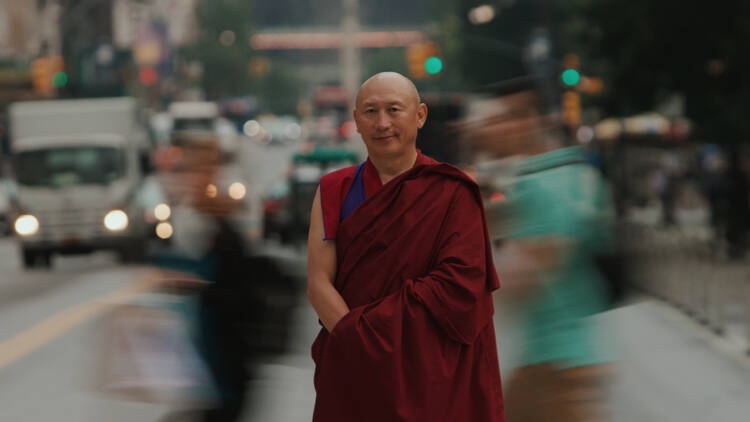 Geshe La stands streetside with traffic blurred in the background.