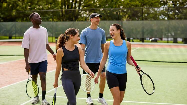 A group of four friends, two men and two women, smile while holding tennis rackets.