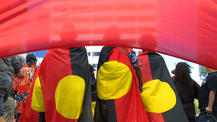 A group of people wearing Aboriginal flags as capes.