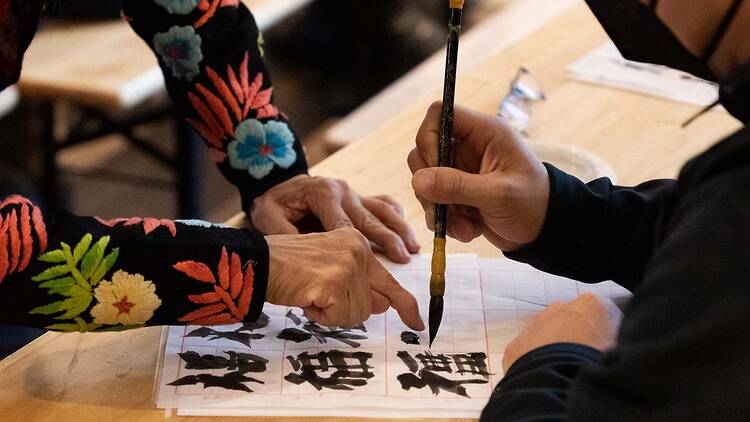 A woman teaches a student how to create Chinese calligraphy.