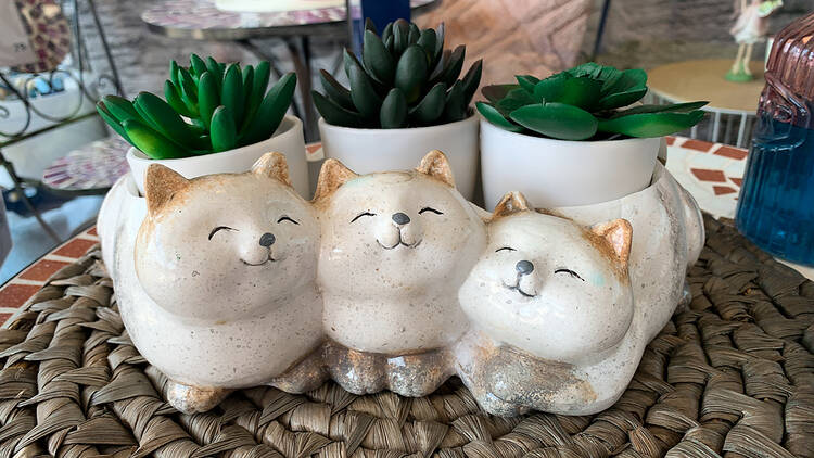 A porcelain planter shaped like three smiling cats, holding artificial plants.