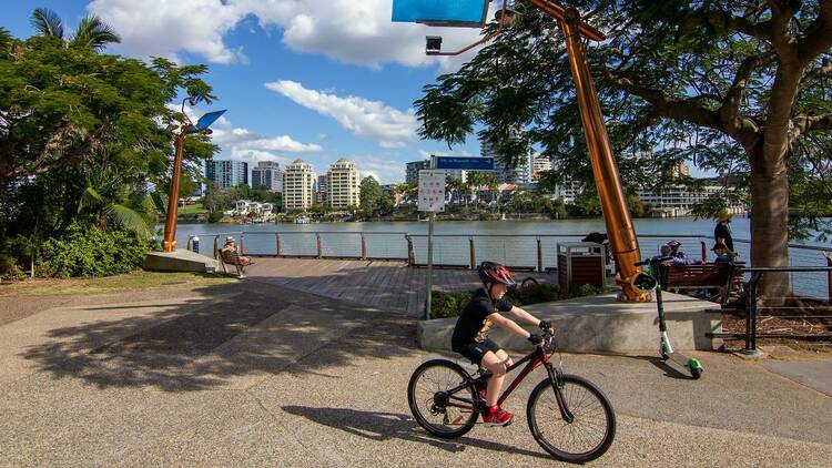 A boy riding a bike along a riverside bikeway