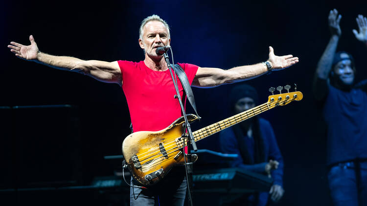 Musician Sting performing on stage with a guitar.