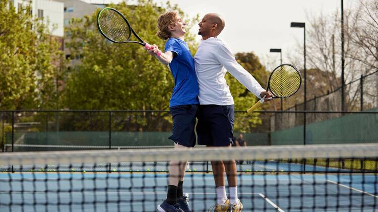 Two friends bumping chests playfully on a tennis court