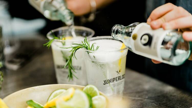StrangeLove tonic water is poured into two Juniperlooza branded gin and tonic cups, garnished with lemon and rosemary.
