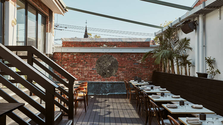 The rooftop at Rufio has a wooden deck with a brick walls and a row of white tables