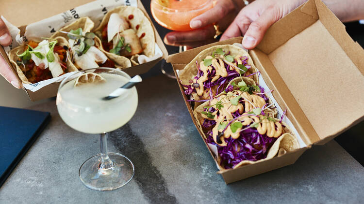 There are two boxes of take away tacos next to two margarita drinks 