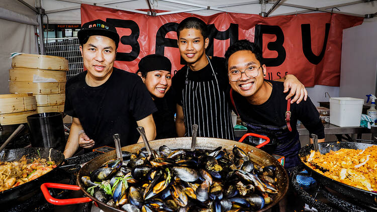 Four chefs crowd around a big dish of mussels.