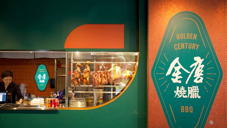 A restaurant counter with roast ducks hanging in the window and a sign saying: 'Golden Century BBQ'