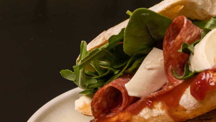 On a white plate there is a baguette filled with salami cheese and spinach