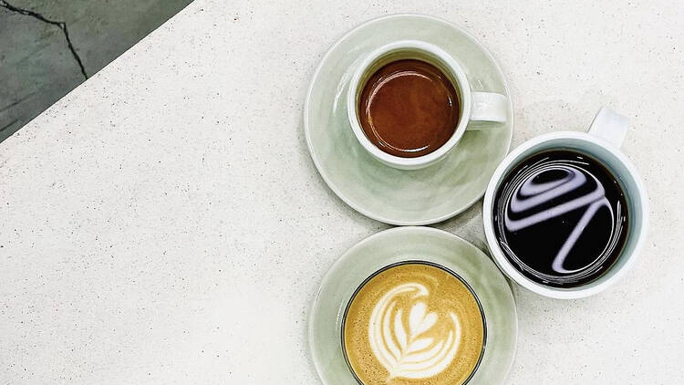 On a white table there are three coffees next to each other, a latte, a long black and a batch brew