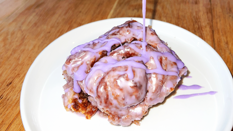 A vegan ube cinnamon bun with pink icing. 