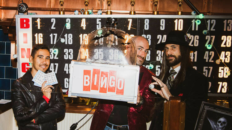 Three people in front of a Bingo board.