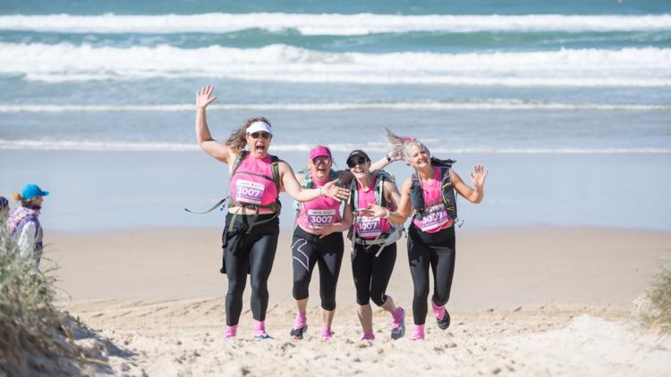 Four woman smiling on a beach doing the Coastrek Mornington Peninsula