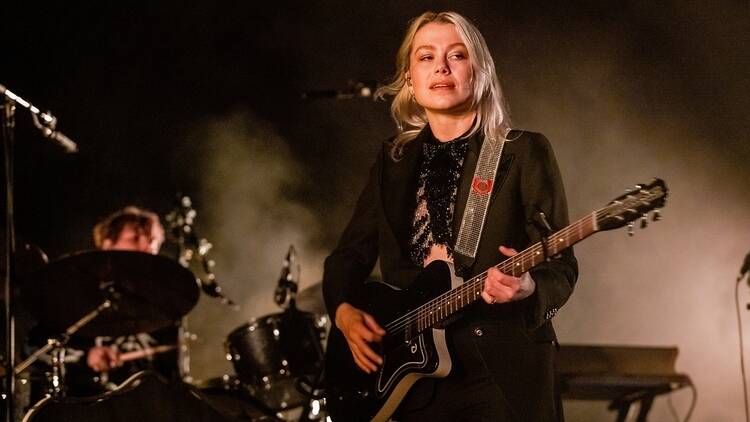 Singer Phoebe Bridgers perf0orming on stage with a guitar.