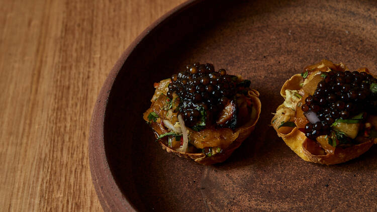 A snack from Serai restaurant sits on a ceramic plate on a wooden table 