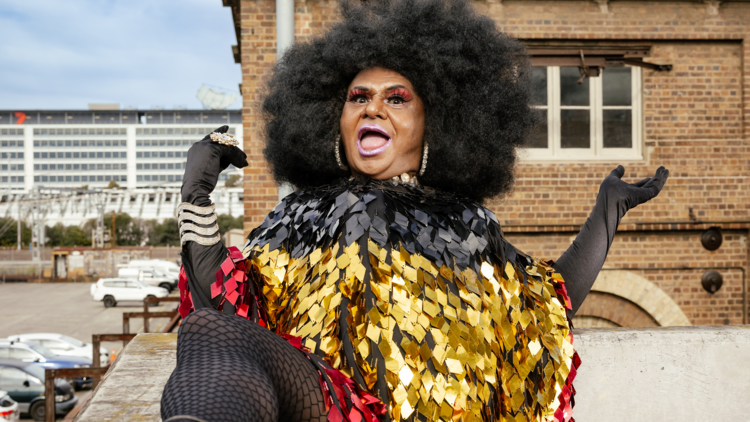 A drag queen in a sparkly outfit in Aboriginal flag colours