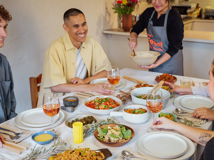 Friends sit around a table hosting a Feast for Freedom with many different plates of food and glasses of wine on the table