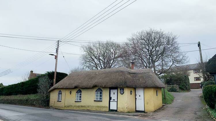 A yellow house on the side of a road with a thatched roof 