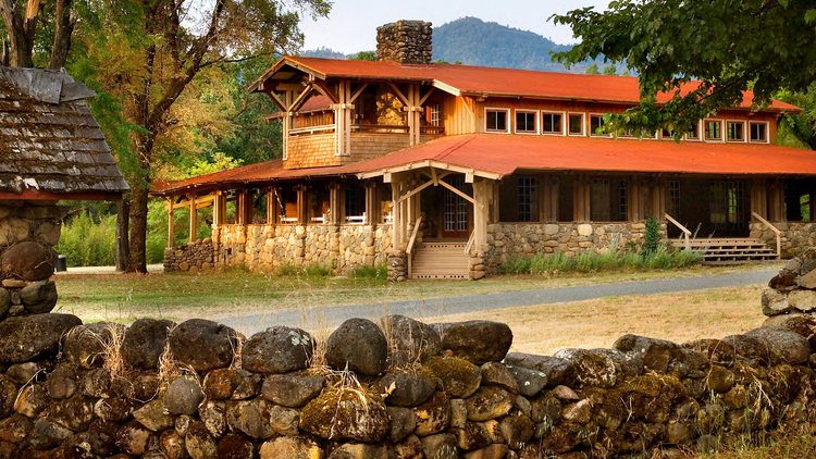 A rustic two-story resort of wood and stone lies behind a wall made of round stones