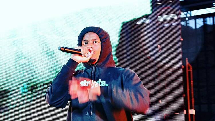 Rapper Denzel Curry wearing a hoodie and performing on stage.