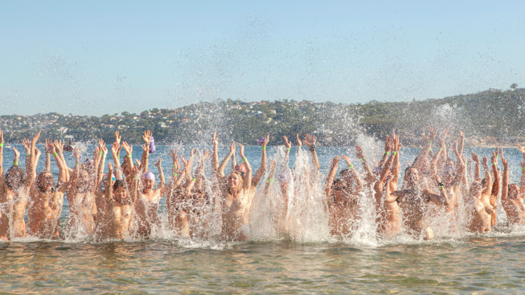 A line of nude people splash water while standing in ocean