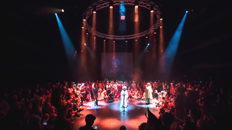 People surround a circle stage drenched in stage lights