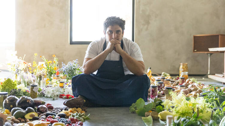 A chef sitting on the floor in the middle of a whole lot of vegetables.